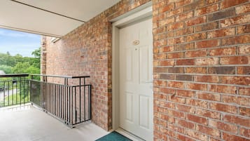 A balcony with a metal railing, a white door, and a brick wall.