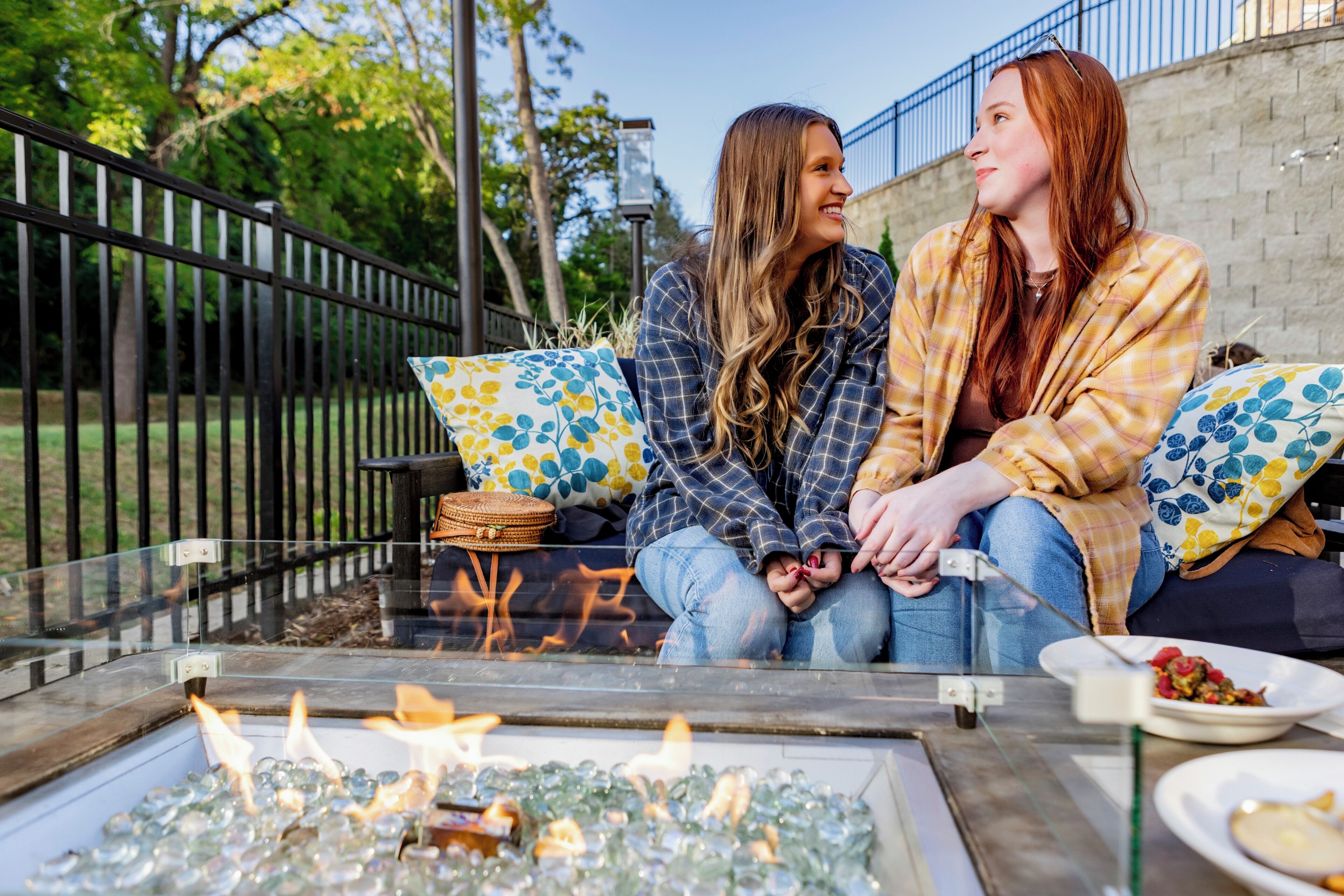 Two individuals seated on a bench outdoors with a fire feature in front of them.