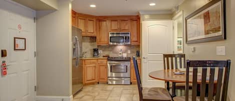 A kitchen with wooden cabinets, a stainless steel refrigerator, a microwave, an oven, and a dining table with chairs.