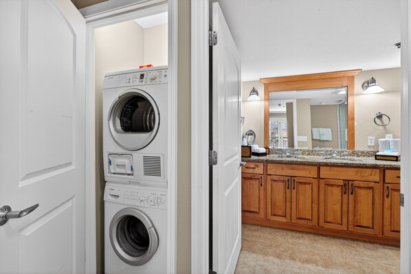 A laundry room with stacked washers and dryers, wooden cabinets, a granite countertop, and a large mirror.