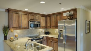 A modern kitchen with wooden cabinets, stainless steel appliances, granite countertops, and a built-in sink.
