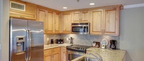 A modern kitchen with stainless steel appliances, wooden cabinets, granite countertops, and a built-in oven.