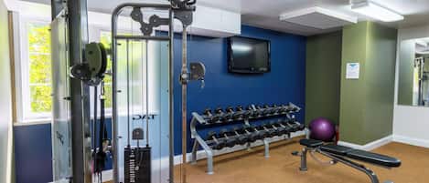 A gym with exercise equipment, dumbbells, a stationary bike, and a wall-mounted TV.