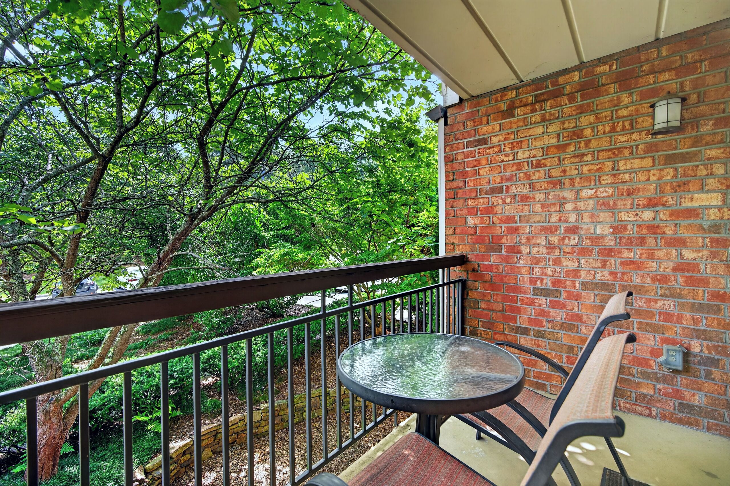 Un balcon avec un mur en briques, une rambarde en métal, une table ronde et un banc.