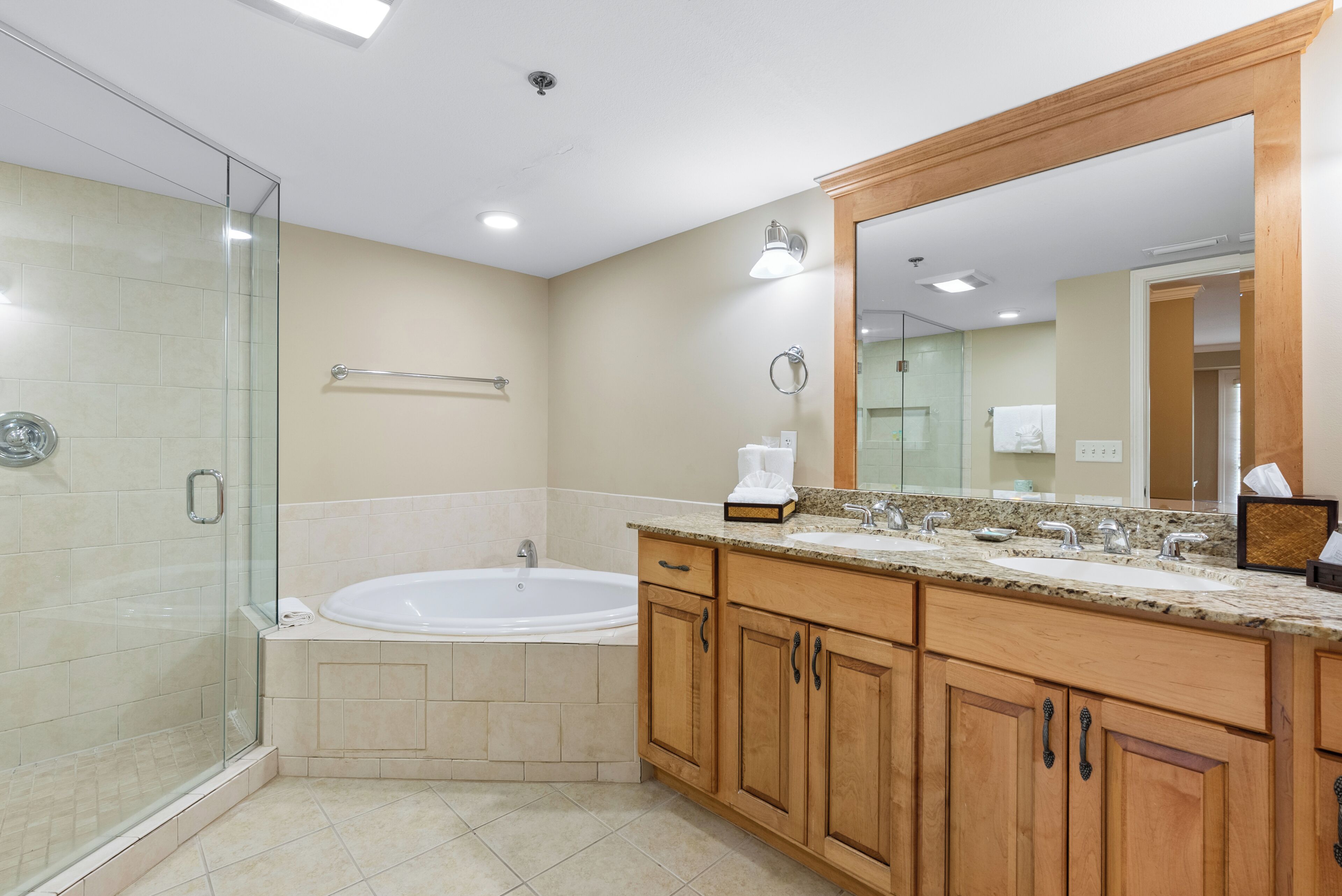 A modern bathroom with a glass shower enclosure, a freestanding bathtub, wooden cabinetry, and a large mirror.