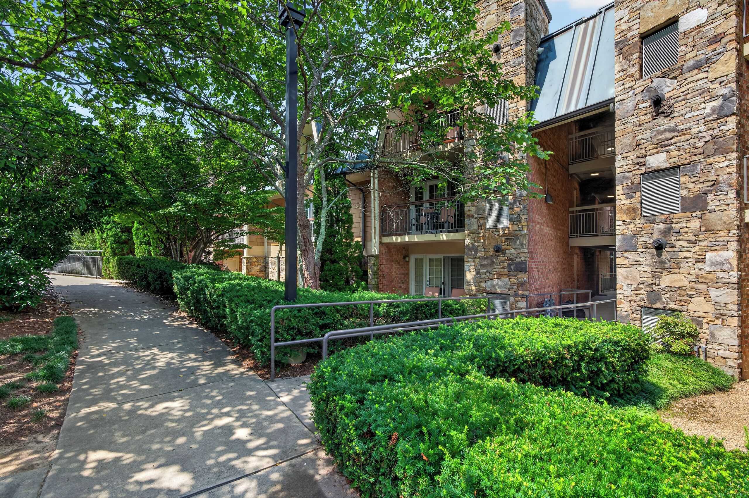 A pathway flanked by well-maintained hedges and a stone building with a balcony.