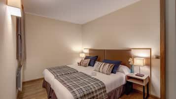 Una cama bien hecha con un edredón escocés, dos lámparas de noche y una mesita con un jarrón y un libro.