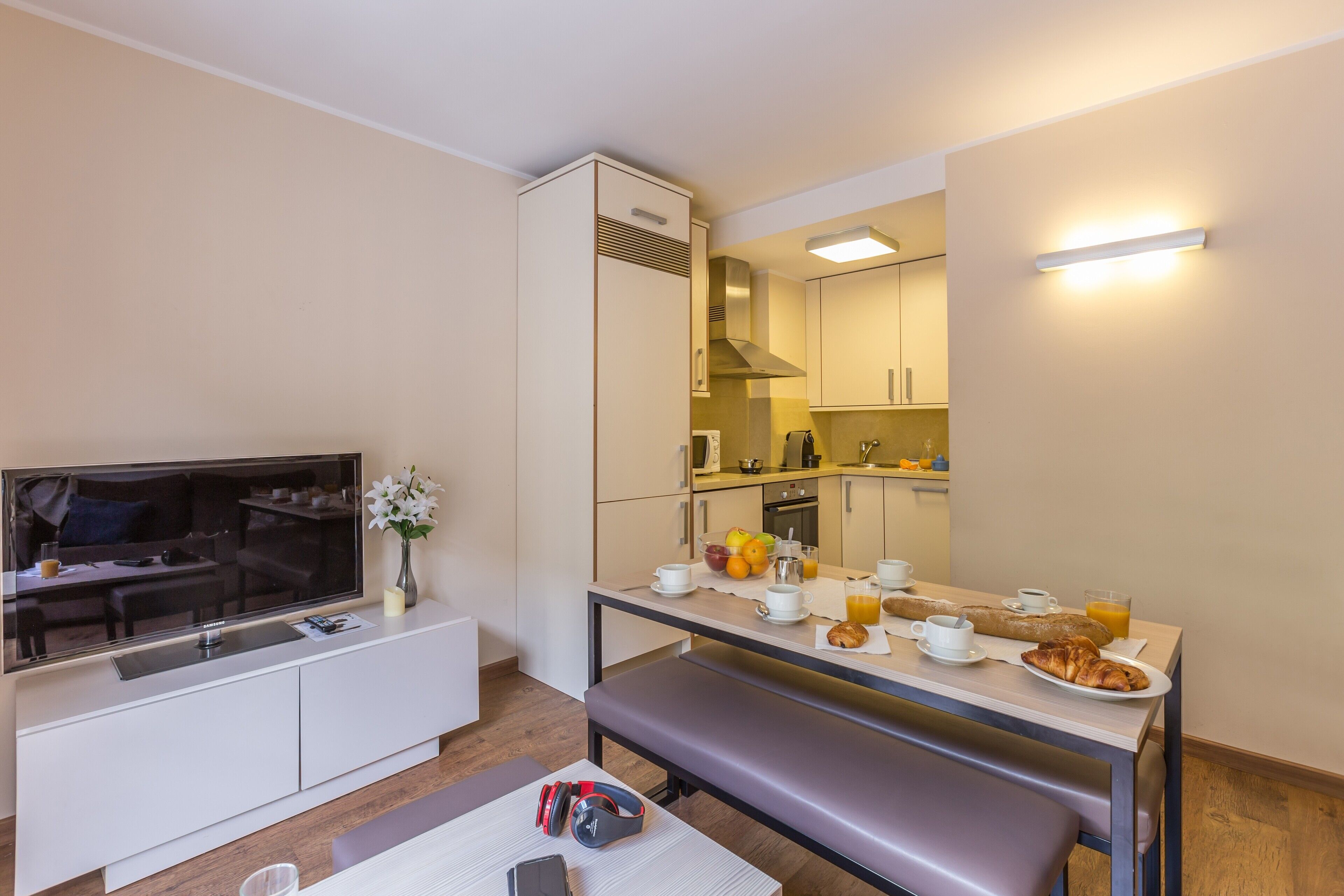 Eine moderne Küche mit Essbereich, einem Flachbildfernseher und einer Frühstücksecke mit Croissants und Orangensaft.