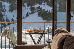 Un balcón con una mesa dispuesta para el desayuno, con vistas a un paisaje montañoso nevado.