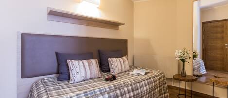 Un dormitorio con cama, almohadas, una mesita de noche con un florero y una puerta de madera.