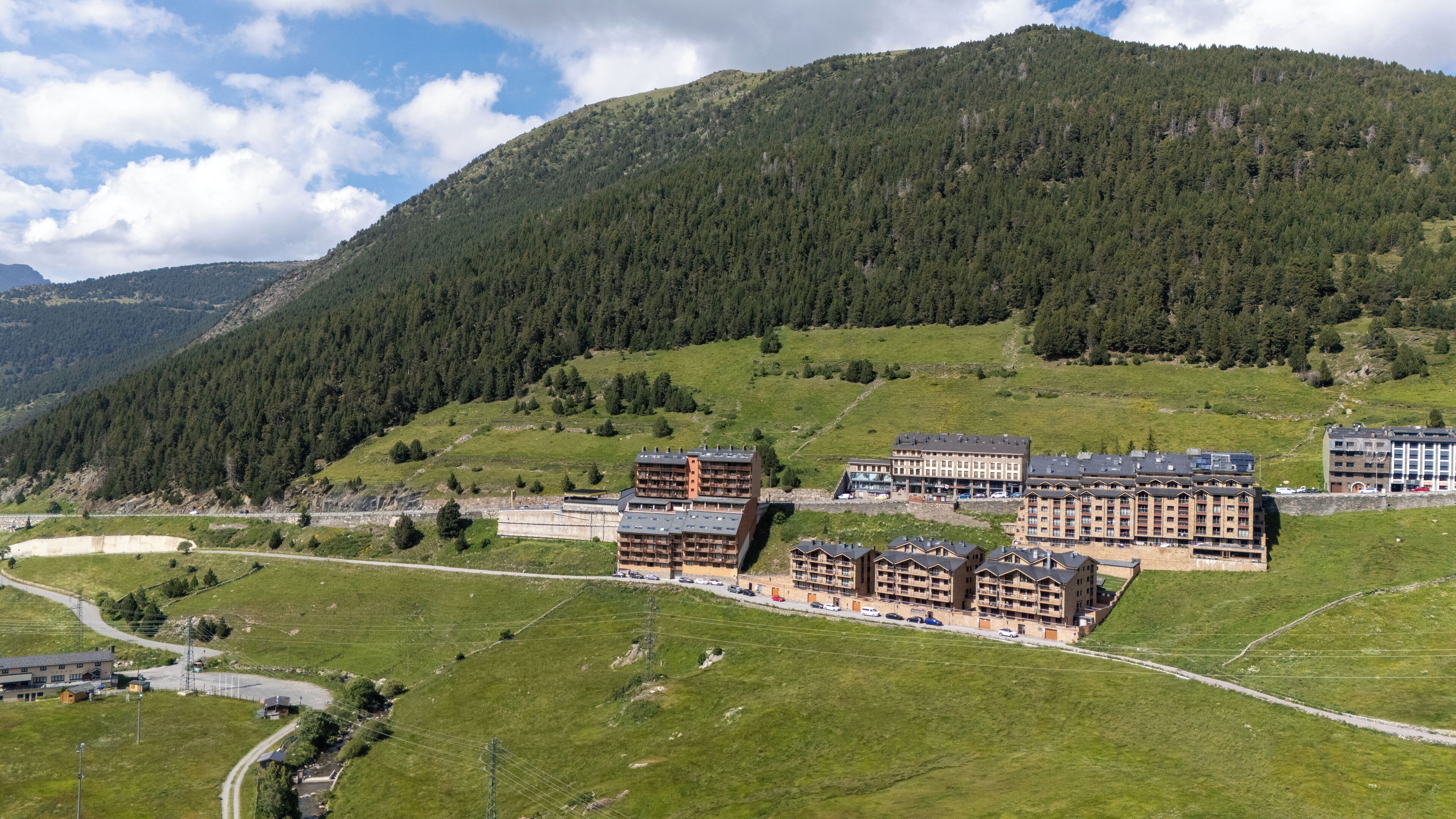 A hotel complex with multiple buildings, surrounded by a mountainous landscape and green fields.