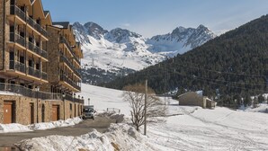 Un immeuble à plusieurs étages doté de balcons, une route pavée et, au loin, des montagnes enneigées.