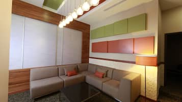 Una habitación de hotel moderna con un sofá modular, una mesa de centro de vidrio y una lámpara de pie.