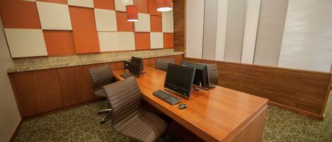 A conference room with a wooden table, multiple chairs, and two computer monitors.