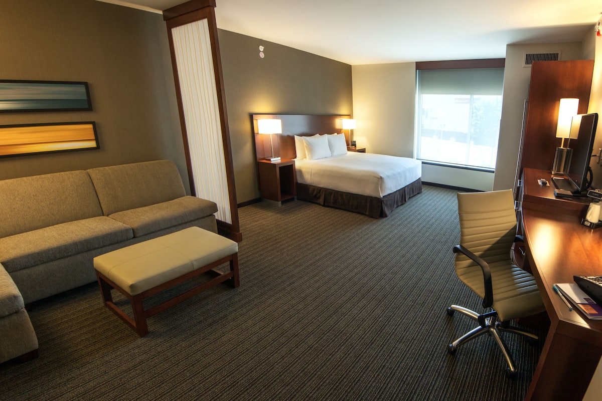 Une chambre d’hôtel équipée d’un canapé, d’un lit, d’un bureau avec une chaise, d’une table de chevet et d’une grande fenêtre.