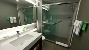 Un baño moderno con ducha envuelta en vidrio, un lavamanos blanco y un espejo sobre él.