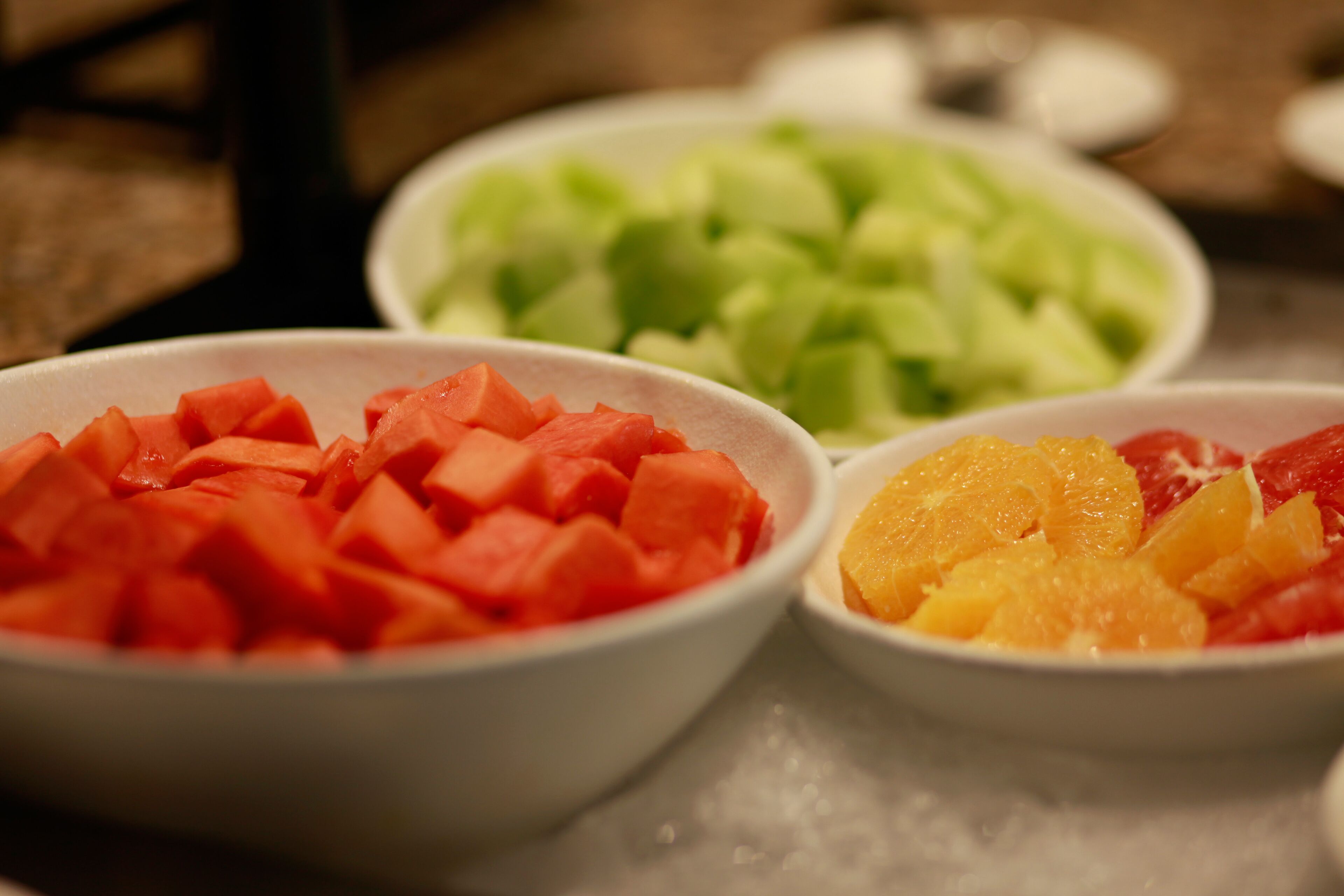 Three bowls of diced fruit on a table.