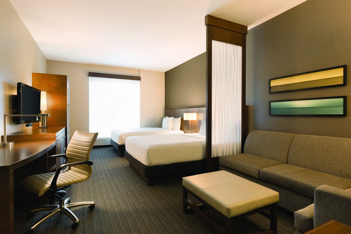 Une chambre d’hôtel équipée d’un bureau, de deux lits, d’un canapé et d’une télévision.