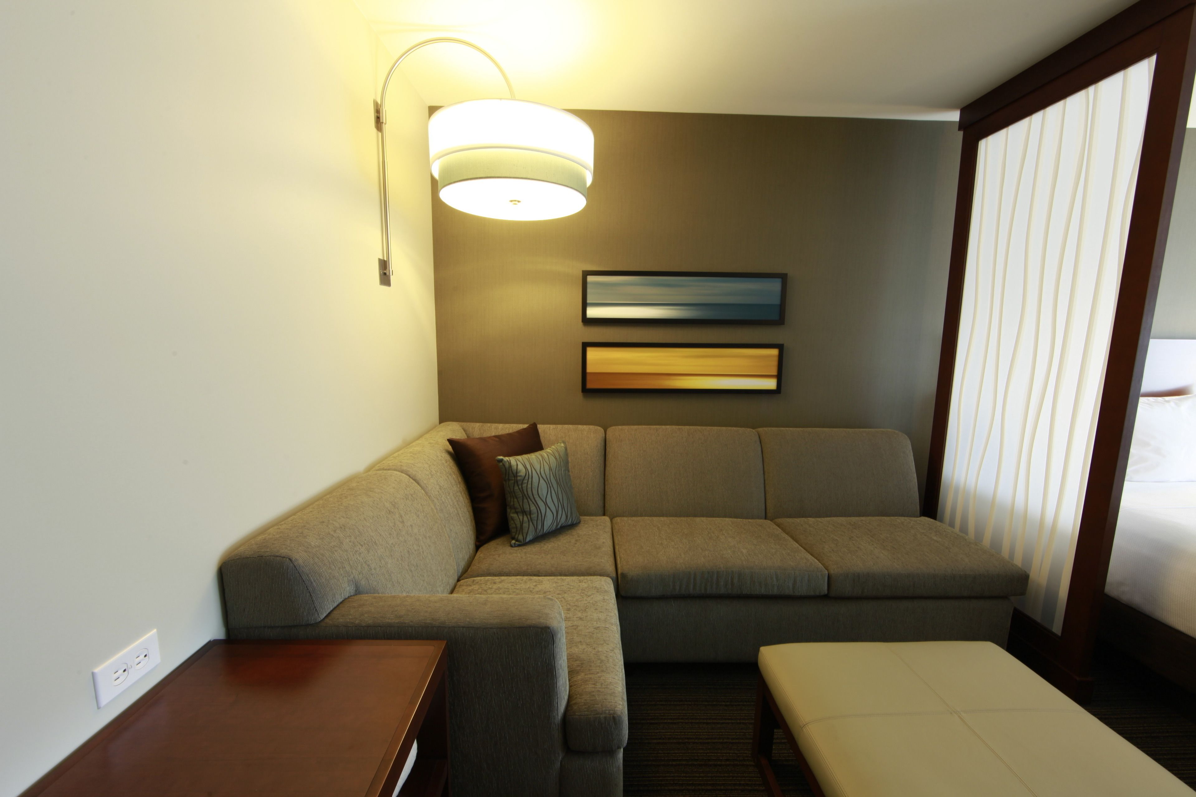 A modern hotel room with a sectional sofa, a small table, and a bed with curtains.
