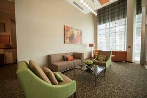Una sala de estar moderna con sofá, sillón y una mesita de centro. Hay un cuadro en la pared y una ventana con persianas.