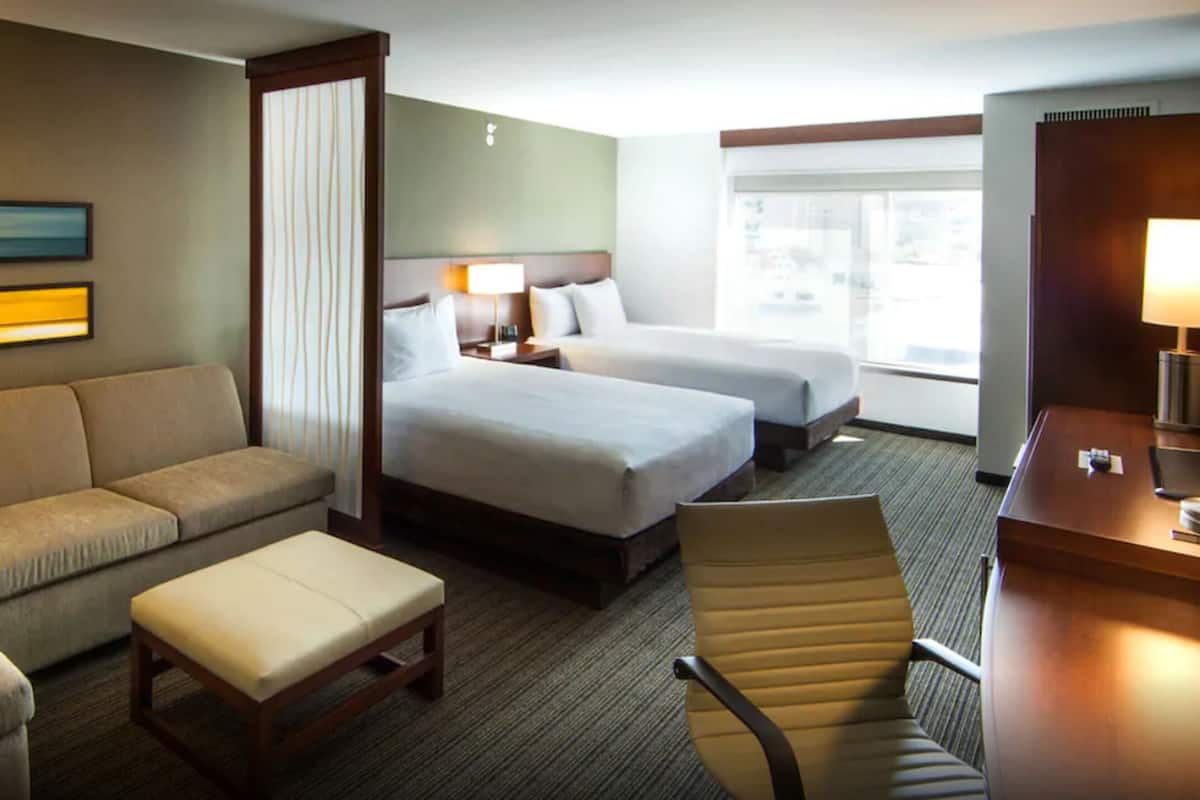 Une chambre d’hôtel avec un canapé, deux lits simples, un bureau et une chaise.