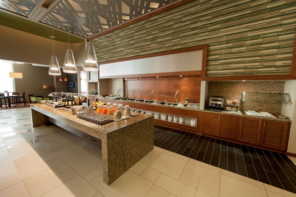 A modern breakfast bar with a granite countertop, overhead lighting, and a variety of breakfast items.