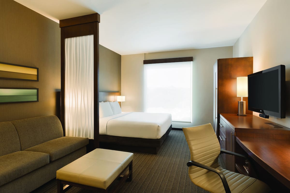 Une chambre d’hôtel avec un lit, un canapé, un bureau, une télévision et une fenêtre avec des rideaux.