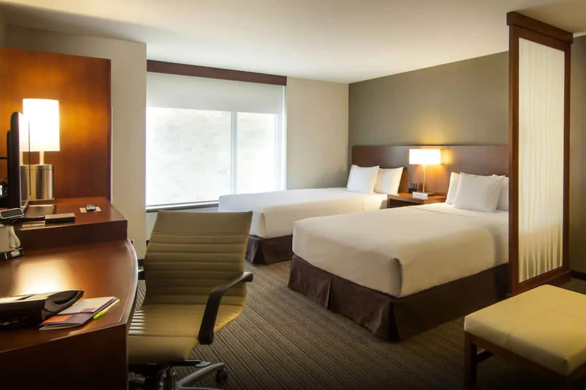 Une chambre d’hôtel avec deux lits, un bureau, une chaise, une petite table et une fenêtre.