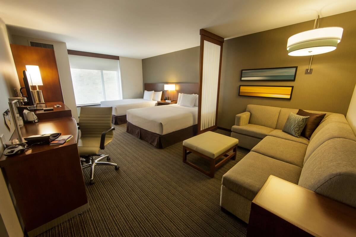 Une chambre d’hôtel avec deux lits, un bureau, une chaise, un canapé et une grande fenêtre.