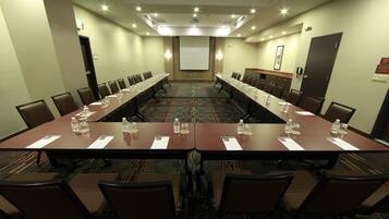 A conference room with a long table, chairs, water bottles, and a projector screen.