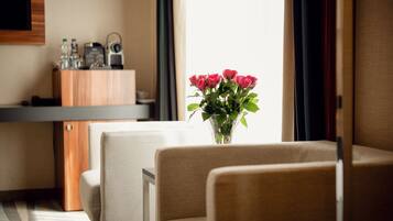 A hotel room with a sofa, a small table with a vase of flowers, a minibar, and a television mounted on the wall.