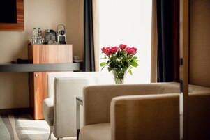 A hotel room with a sofa, a small table with a vase of flowers, a minibar, and a television mounted on the wall.