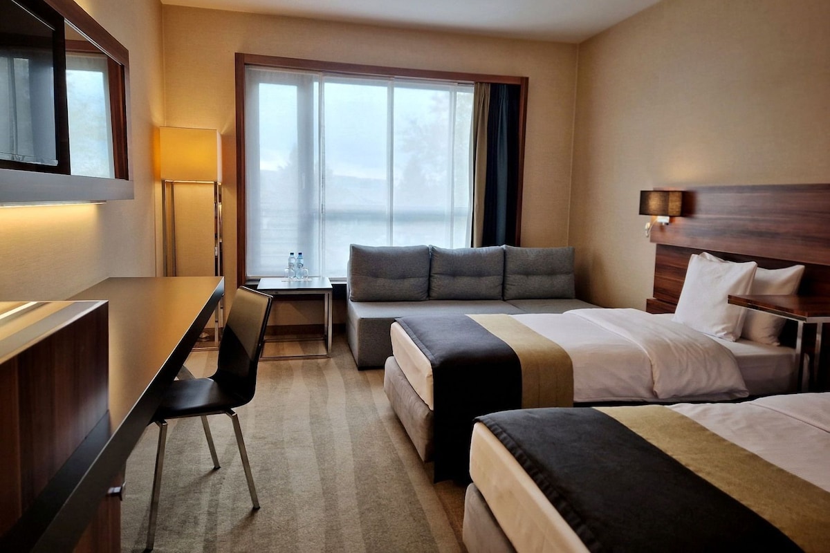 A hotel room with a bed, a desk, a chair, and a window with curtains.