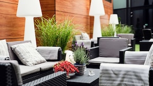 Een terras met rieten meubels, witte lampen en potplanten.
