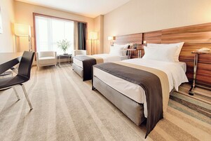 A hotel room with a bed, two bedside tables, a desk, a chair, and a window with curtains.
