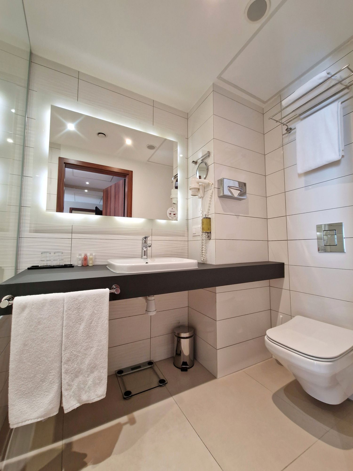 Un baño moderno con un espejo grande, un lavabo, un inodoro y un perchero para toallas.