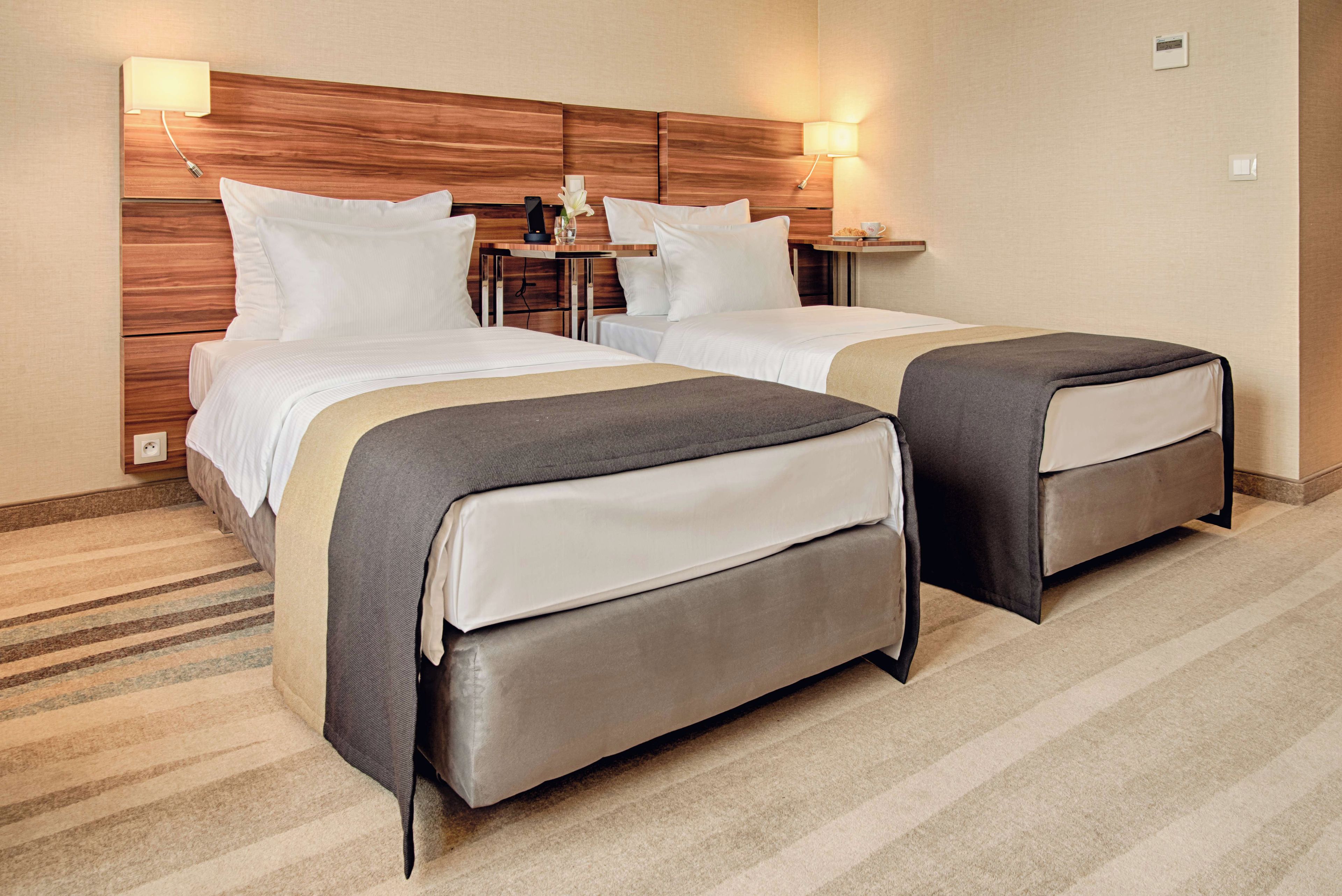 A hotel room with two beds, a wooden headboard, bedside tables with lamps, and a striped carpet.