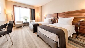 Een hotelkamer met twee bedden, een bureau, een stoel, een lamp en een raam met gordijnen.