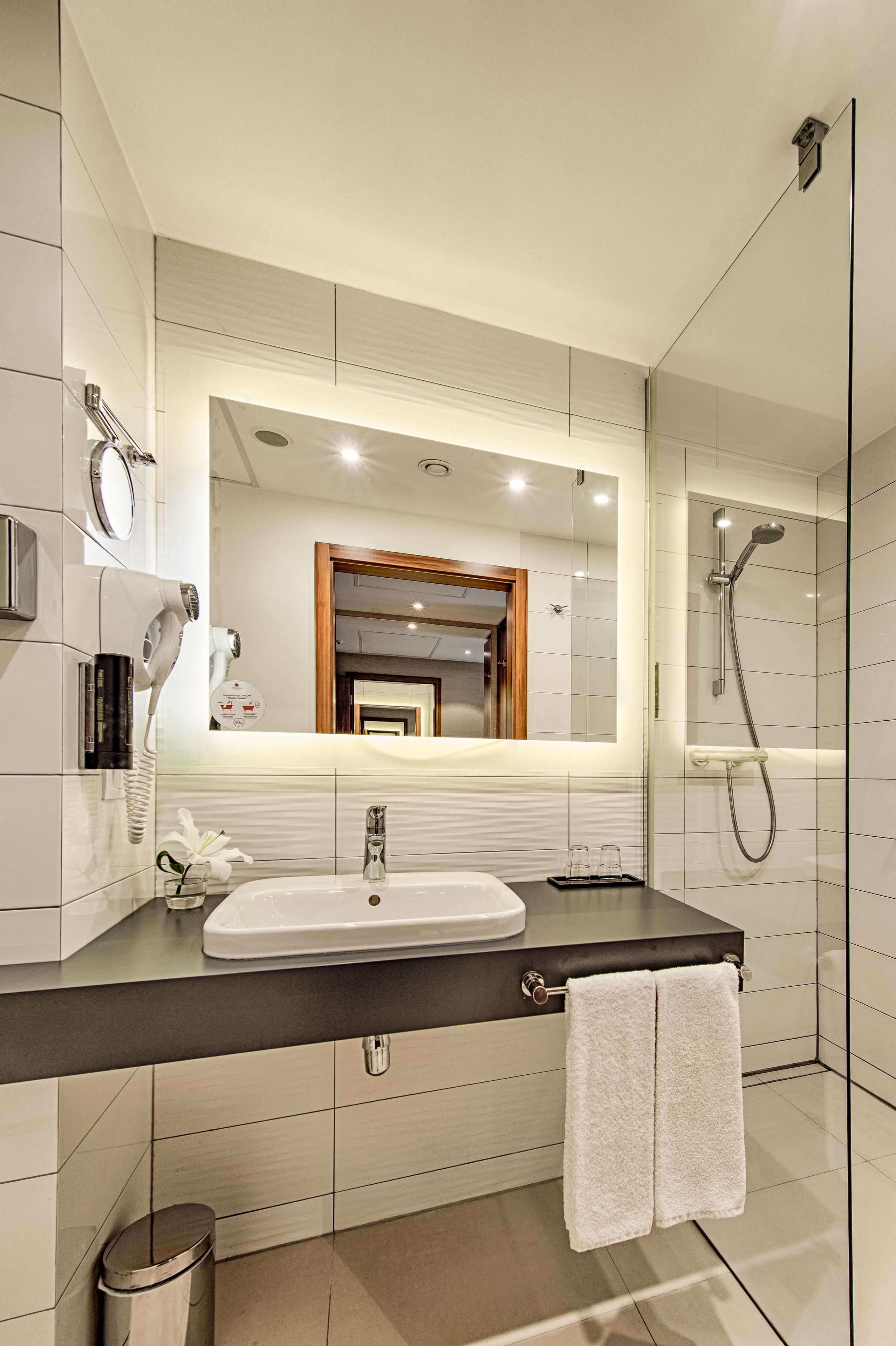 A modern bathroom with a large mirror, a sink, a shower, and a hairdryer.