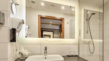 A modern bathroom with a large mirror, a sink, a shower, and a hairdryer.