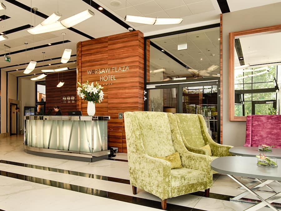 Un espace d’accueil avec un comptoir de réception en bois, un fauteuil vert et une table ronde agrémentée d’un vase de fleurs.
