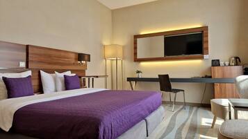 A hotel room with a large bed, a desk with a chair, a TV, and a lamp.