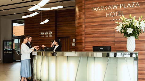 Een receptiebalie in het Warsaw Plaza Hotel, met een wand van hout, een klok en een bloevas.