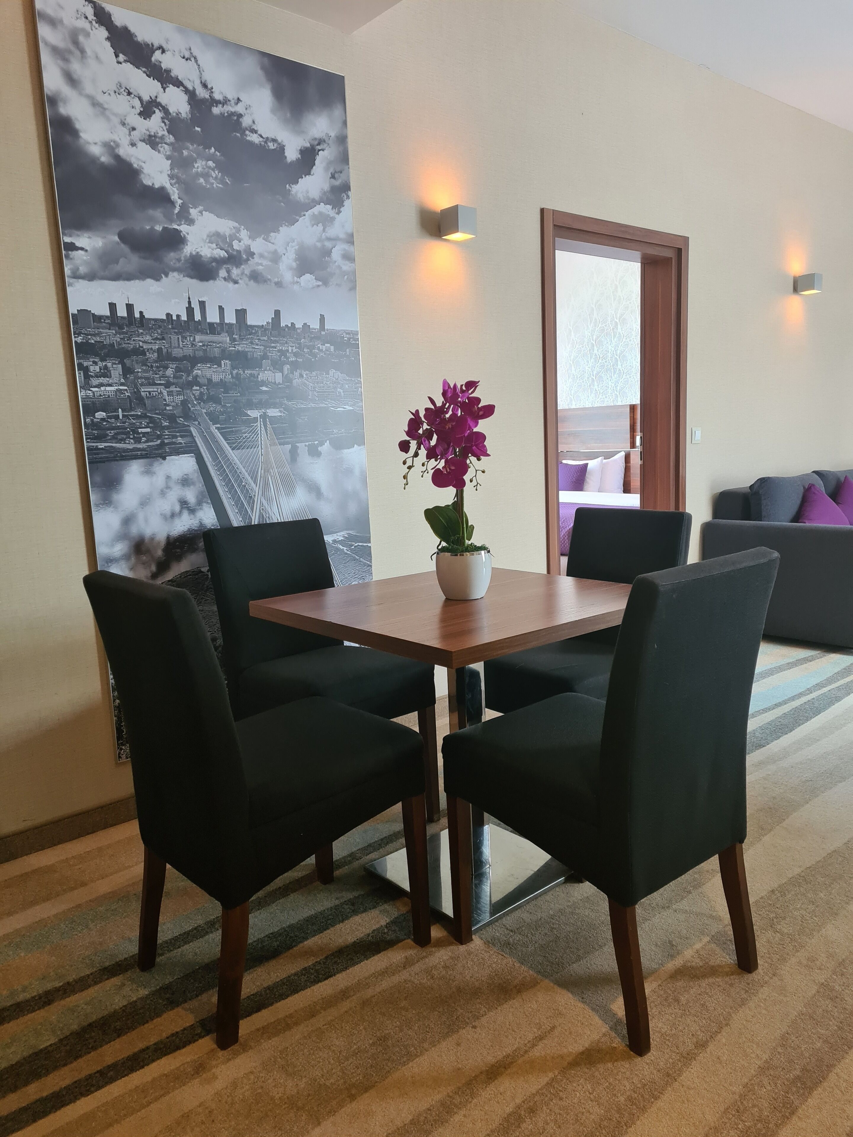 Un comedor con una mesa y sillas, una orquídea en maceta y un cartel con vistas a la ciudad en la pared.