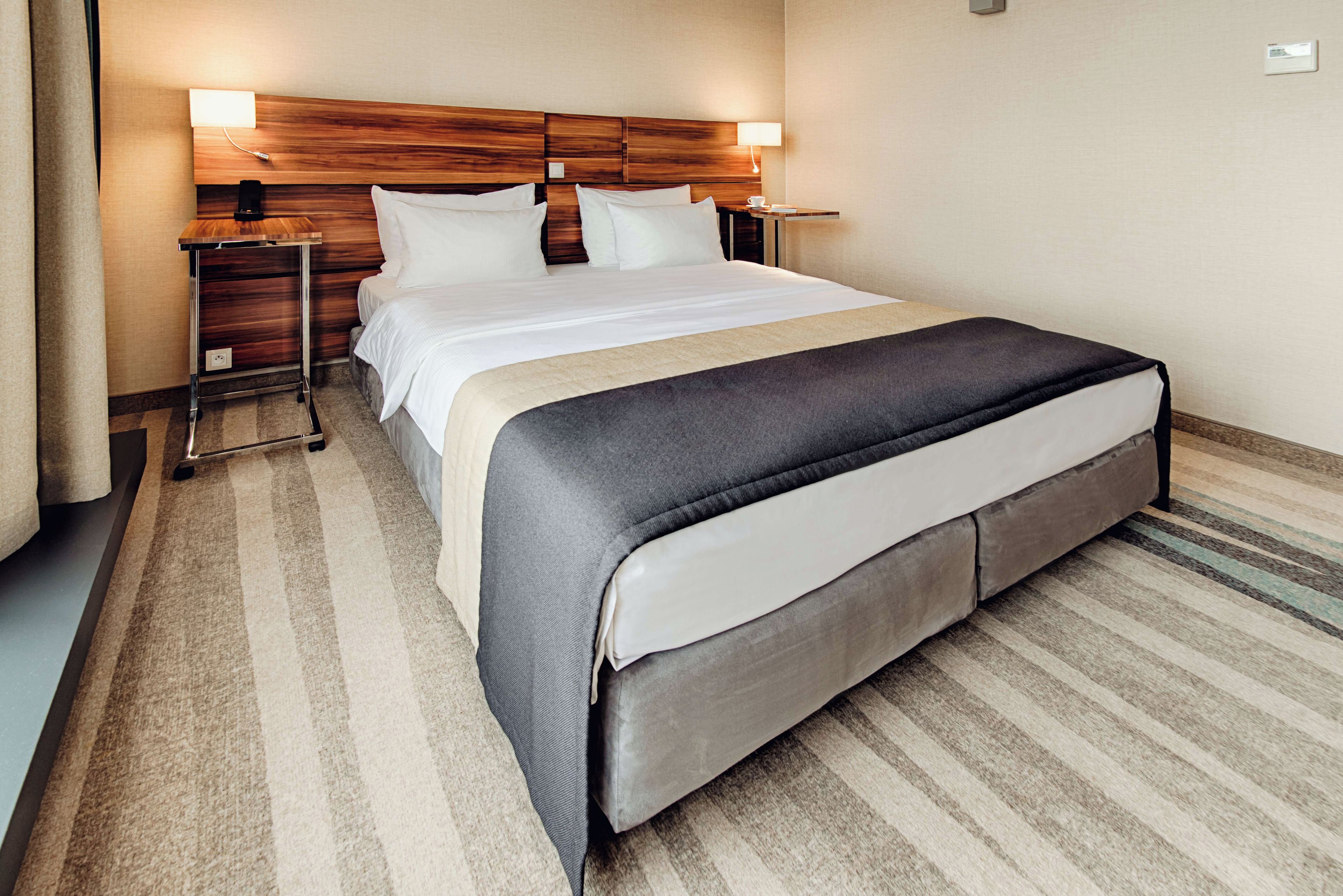 Een hotelkamer met een groot bed, een houten hoofdbord, nachtkastjes en een nachtkast.