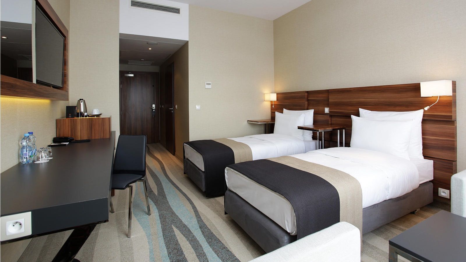 Une chambre d’hôtel avec deux lits, un bureau, une chaise et un mini-bar.