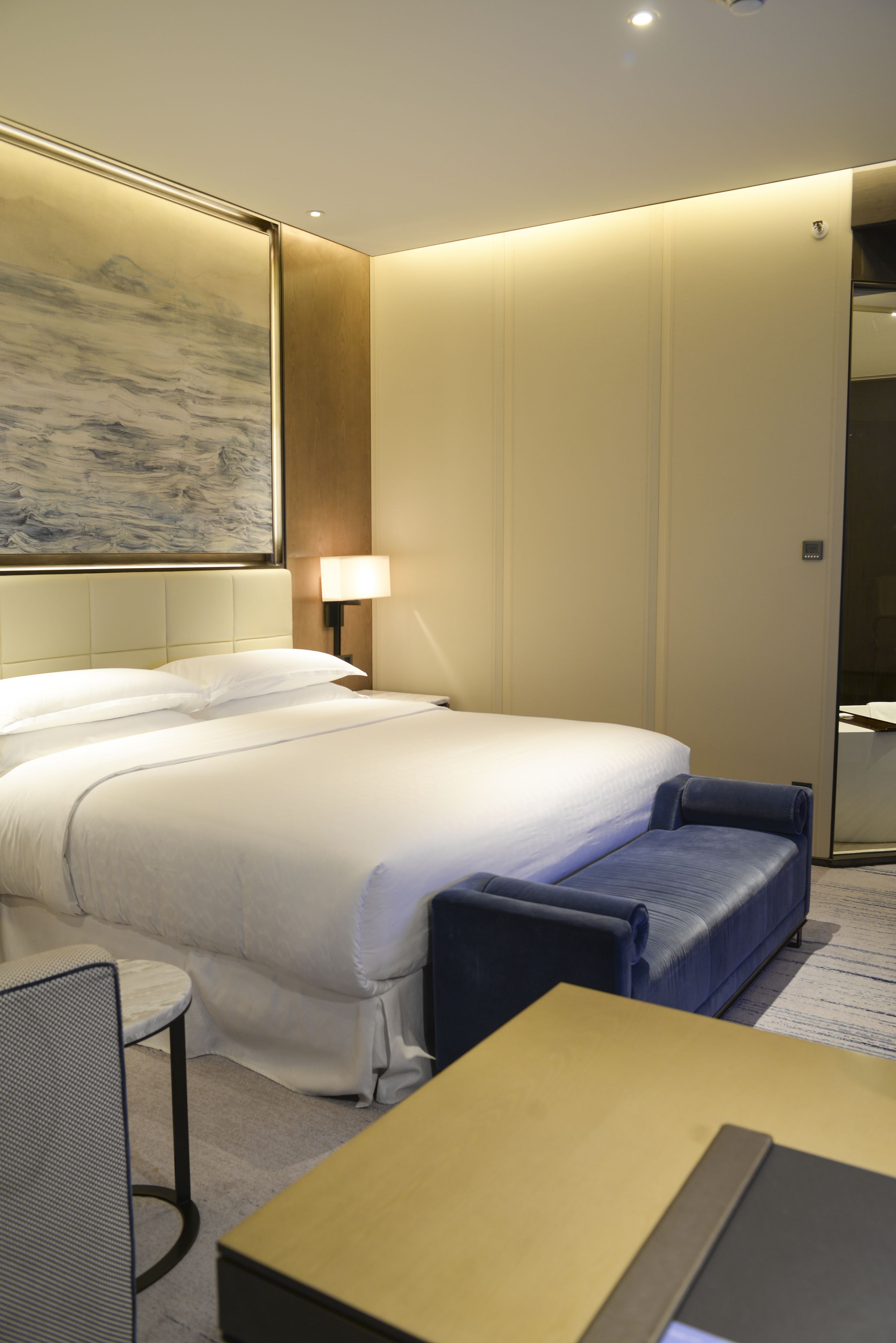 A hotel room with a large bed, a desk, a chair, and a lamp.