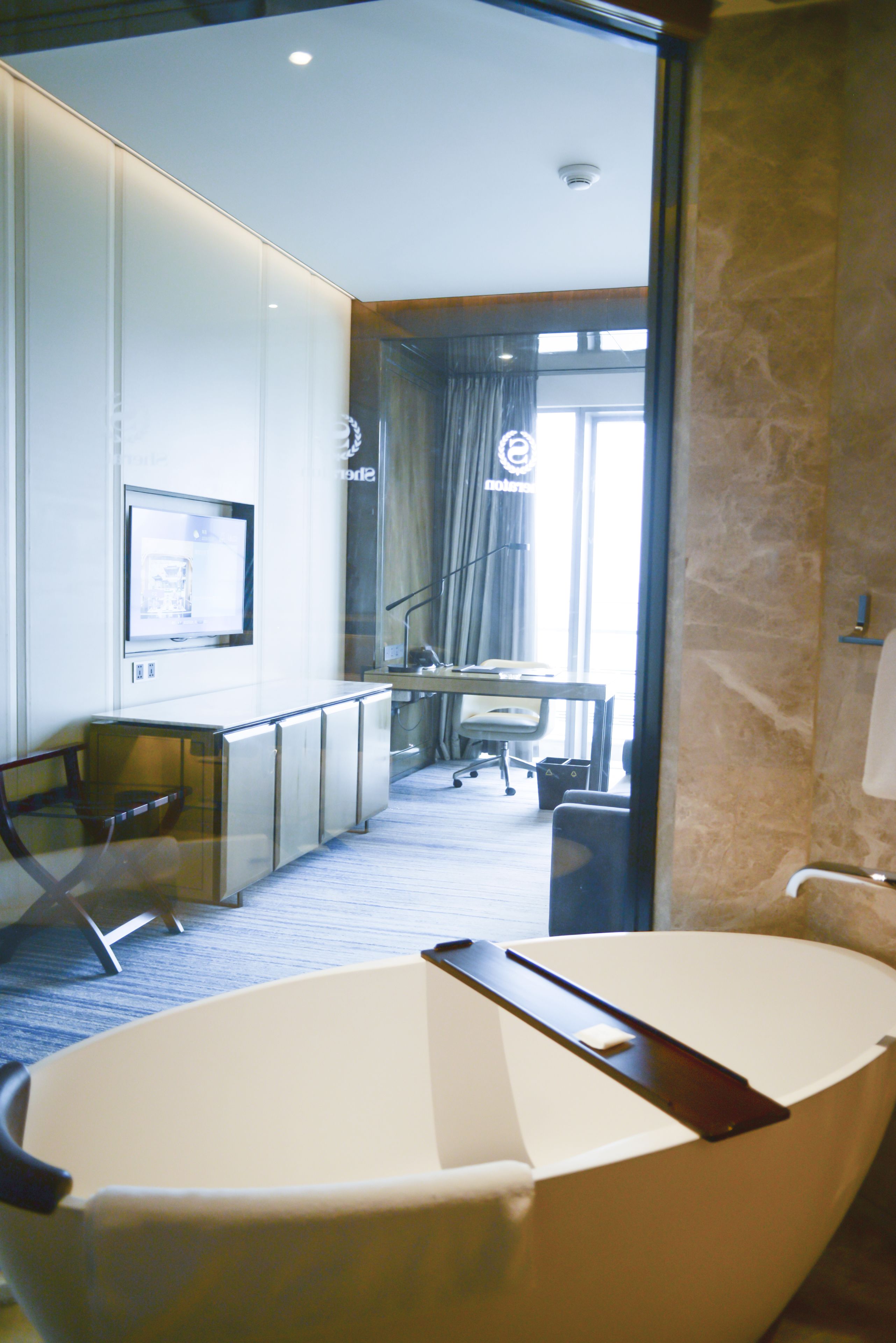 Una habitación de hotel moderna con separador de vidrio, televisor de pantalla plana, escritorio y una silla.