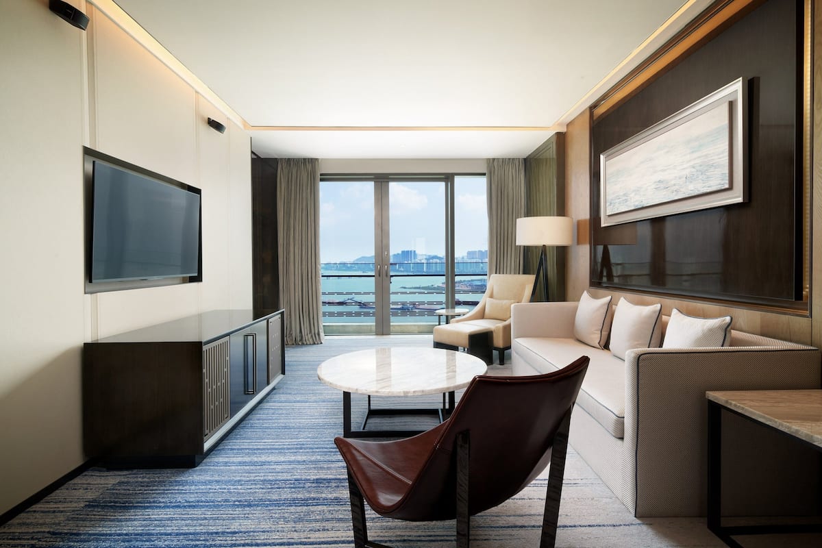 Ein modernes Hotelzimmer mit großem Fenster, Flachbildfernseher, Sofa, Couchtisch und Sessel.