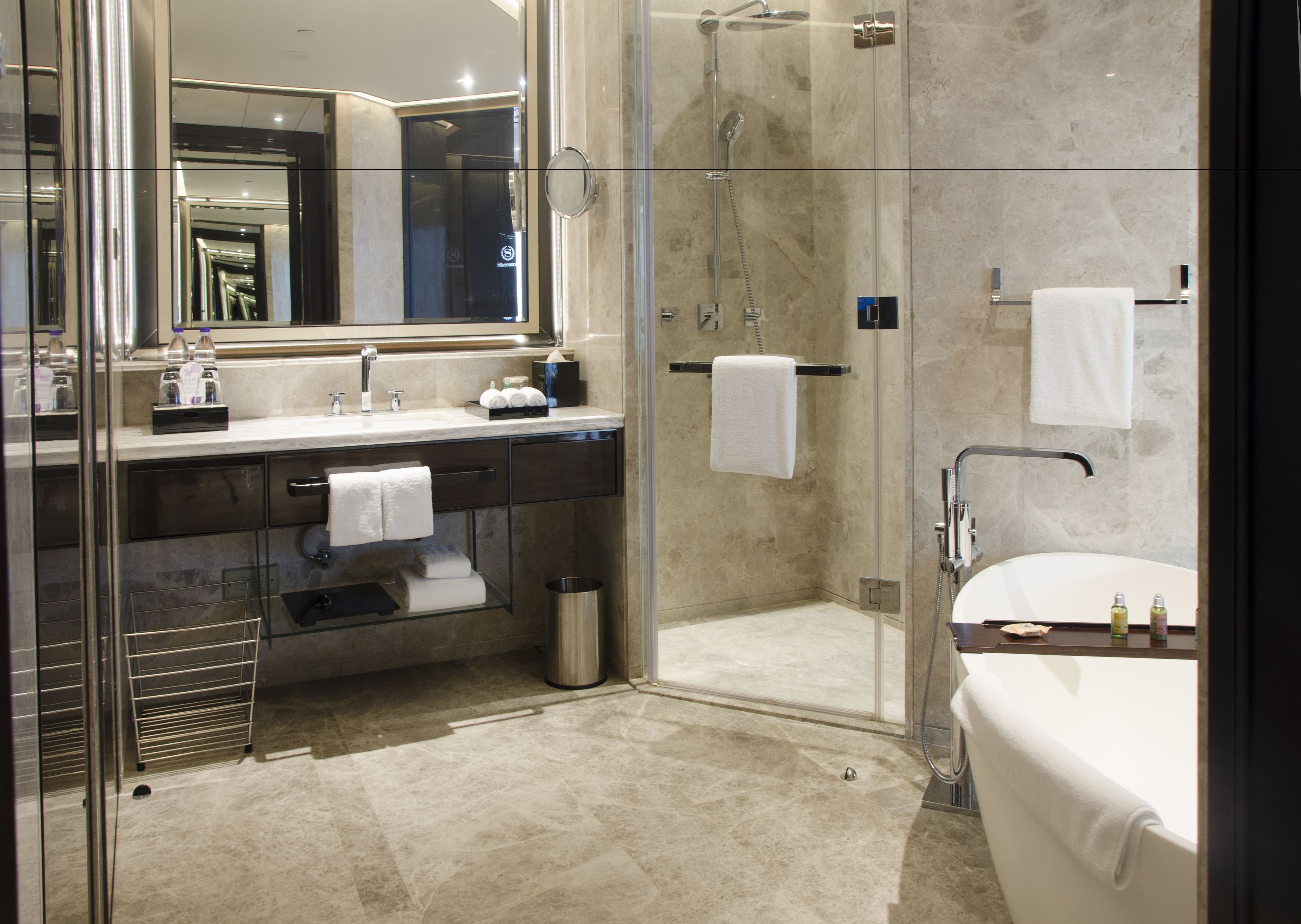 A modern bathroom with a glass-enclosed shower, a large mirror, a bathtub, and a vanity with a sink and towel rack.